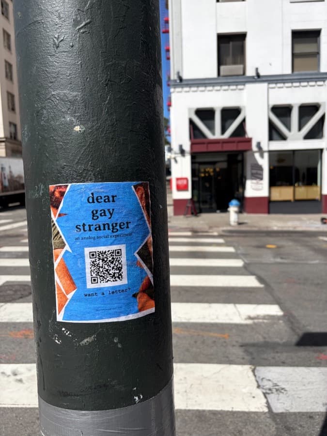 Dear Gay Stranger sticker on a green utility pole by a crosswalk